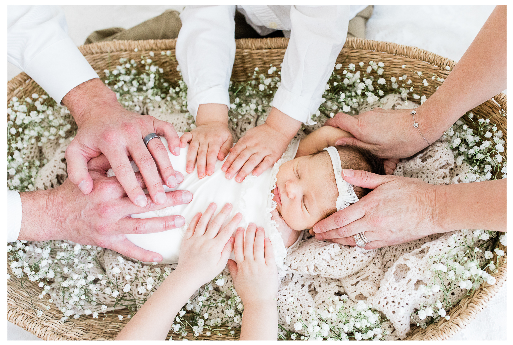 A newborn baby girl asleep in a basket with her family's hands gently holding her.