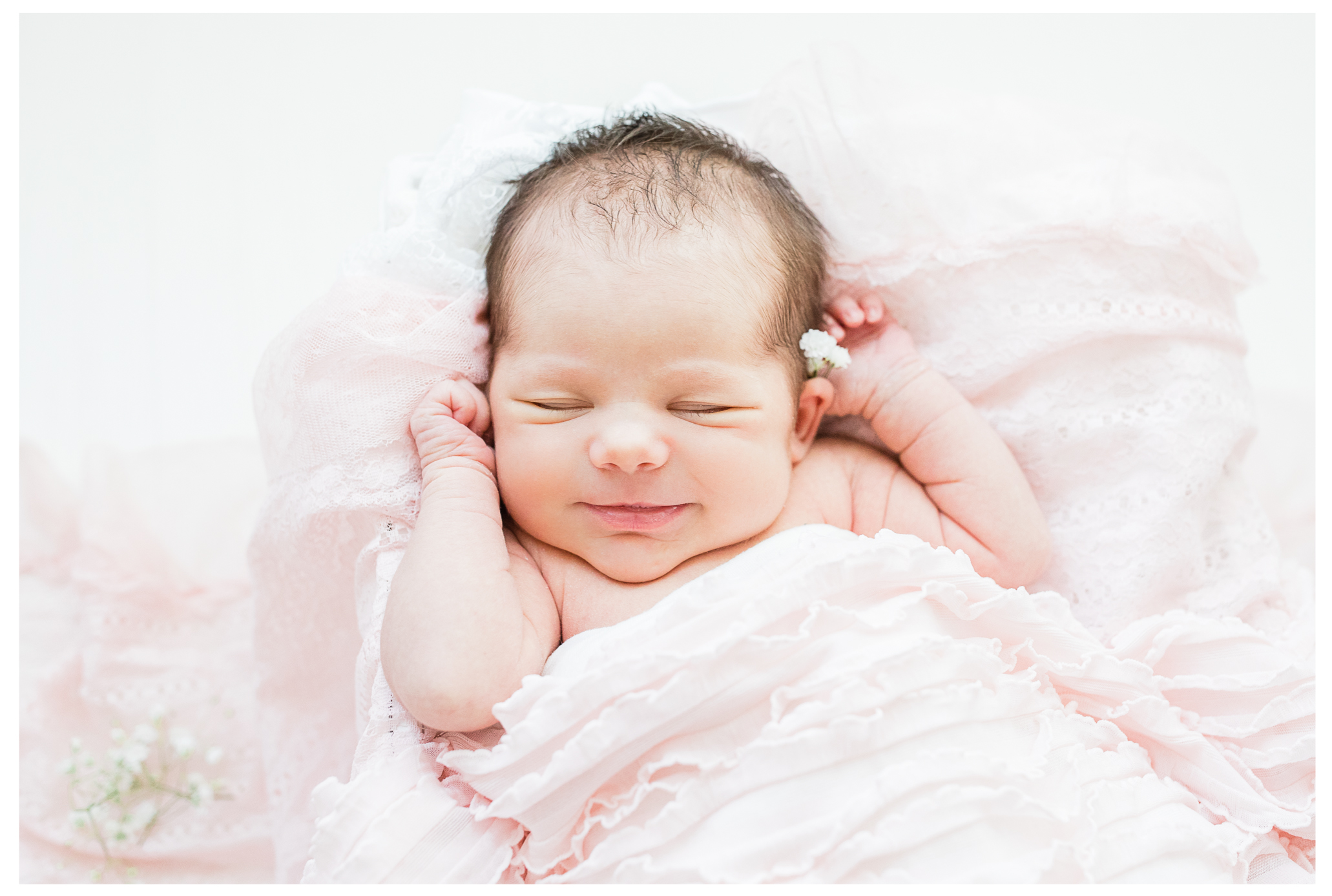 A sleeping newborn girl smiling with baby's breath in her ear