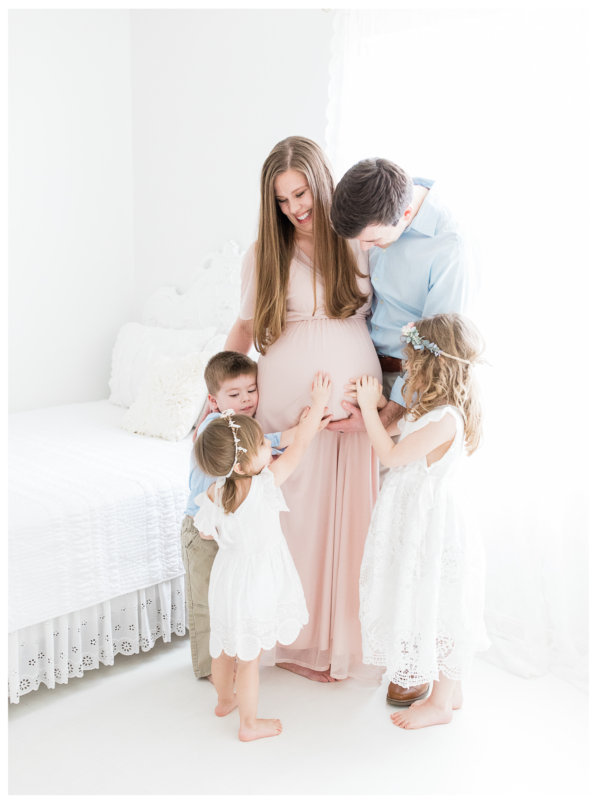 An expecting mother smiling as her husband and three young children embrace her baby bump