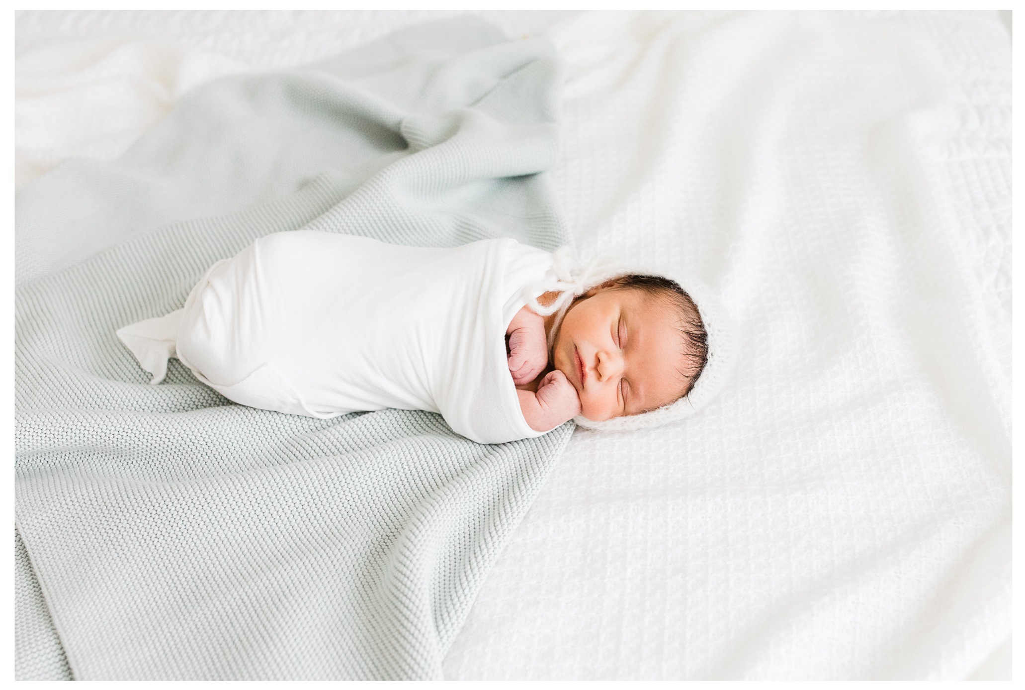 A swaddled baby boy sleeping on a soft blanket while wearing a knit bonnet