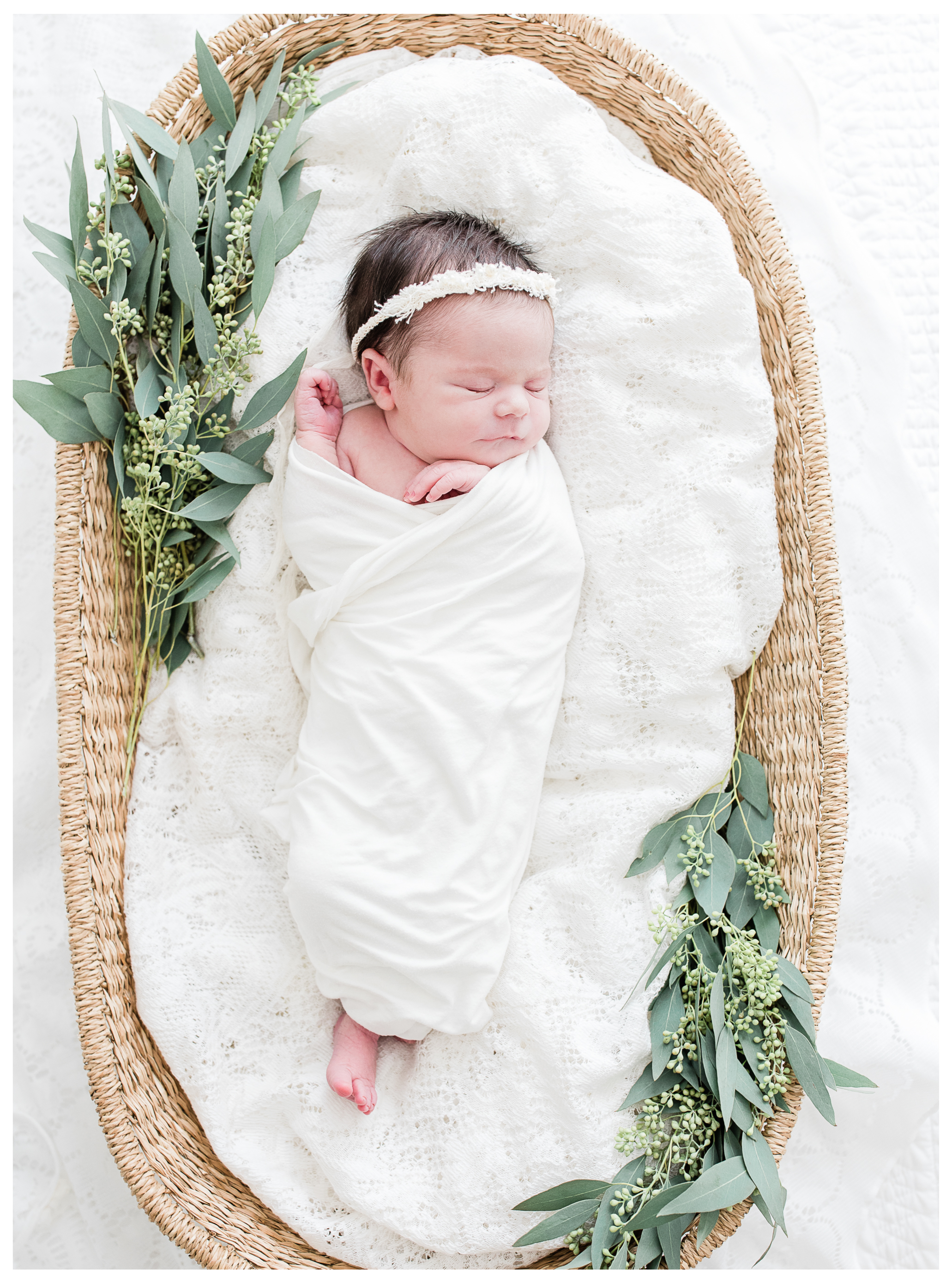 Swaddled newborn girl sleeping in a basket with fresh greenery