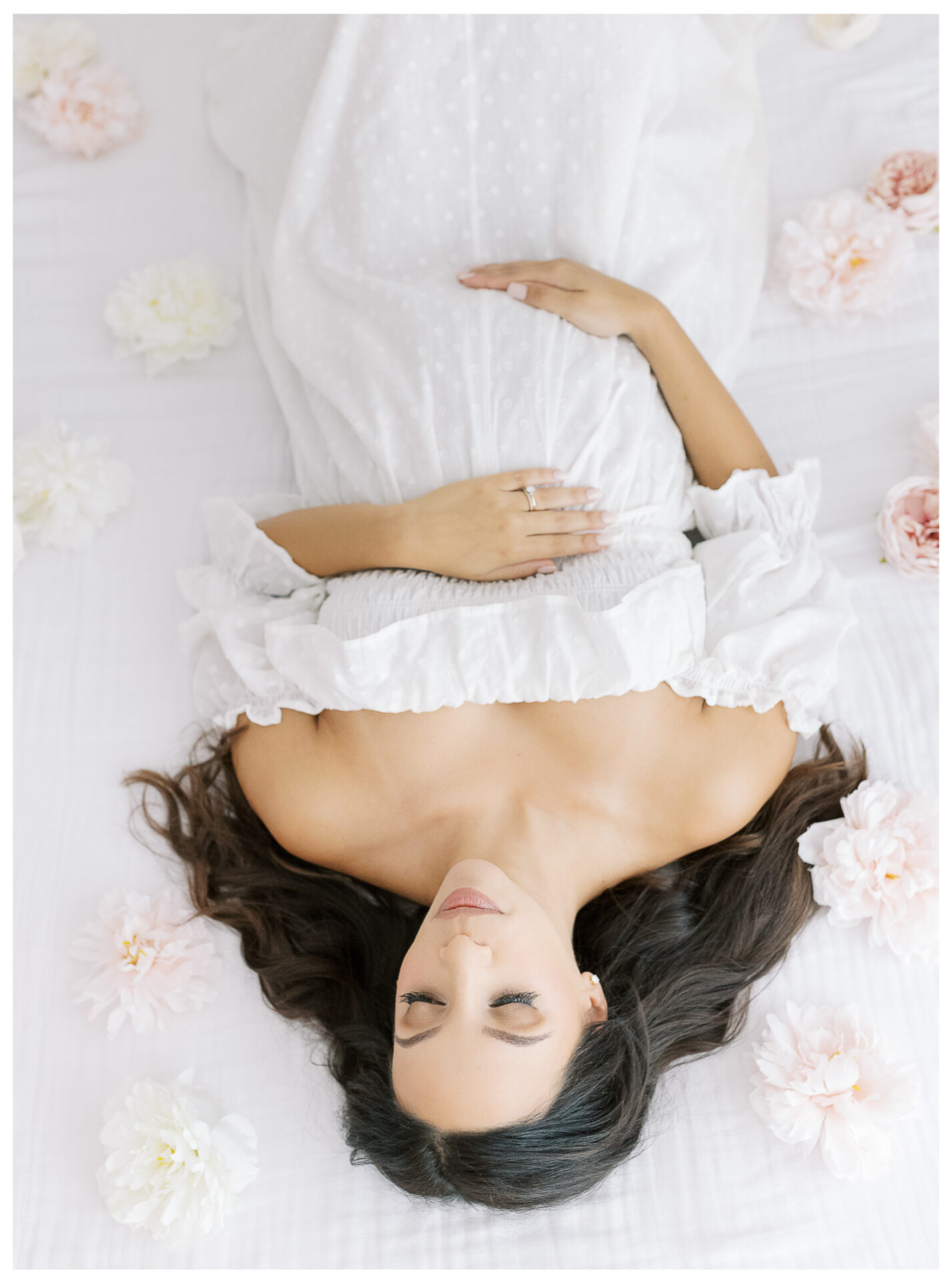 Winter Freire Photography | Natural Light Studio Maternity Session in Dayton, OH | Mama-to-be laying down on a white bed surrounded by flowers