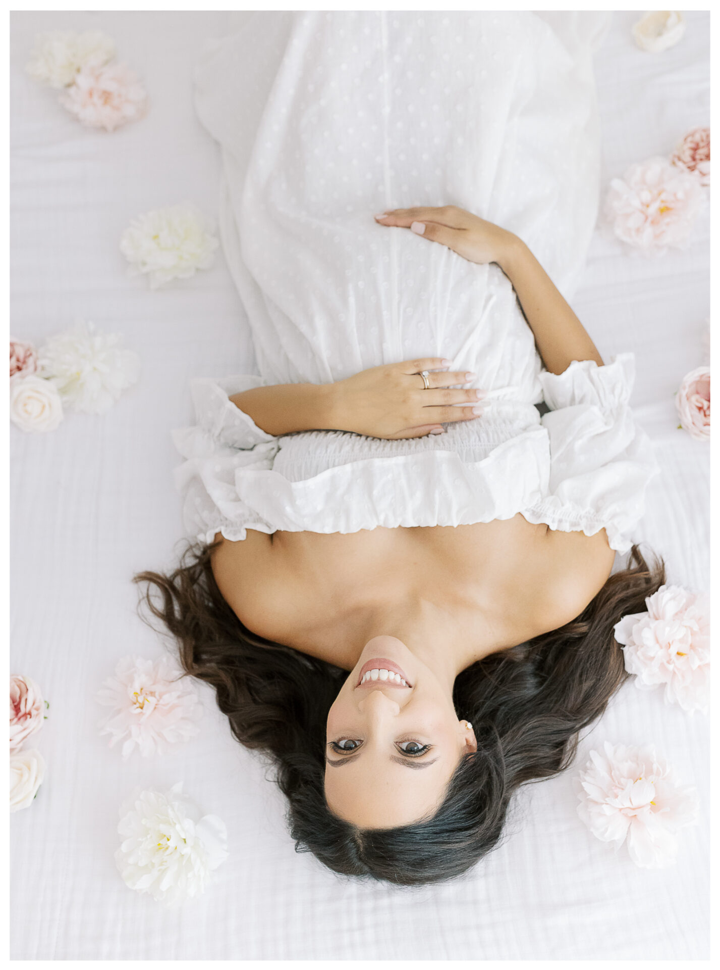 Winter Freire Photography | Natural Light Studio Maternity Session in Dayton, OH | Mama-to-be laying down on a white bed surrounded by flowers