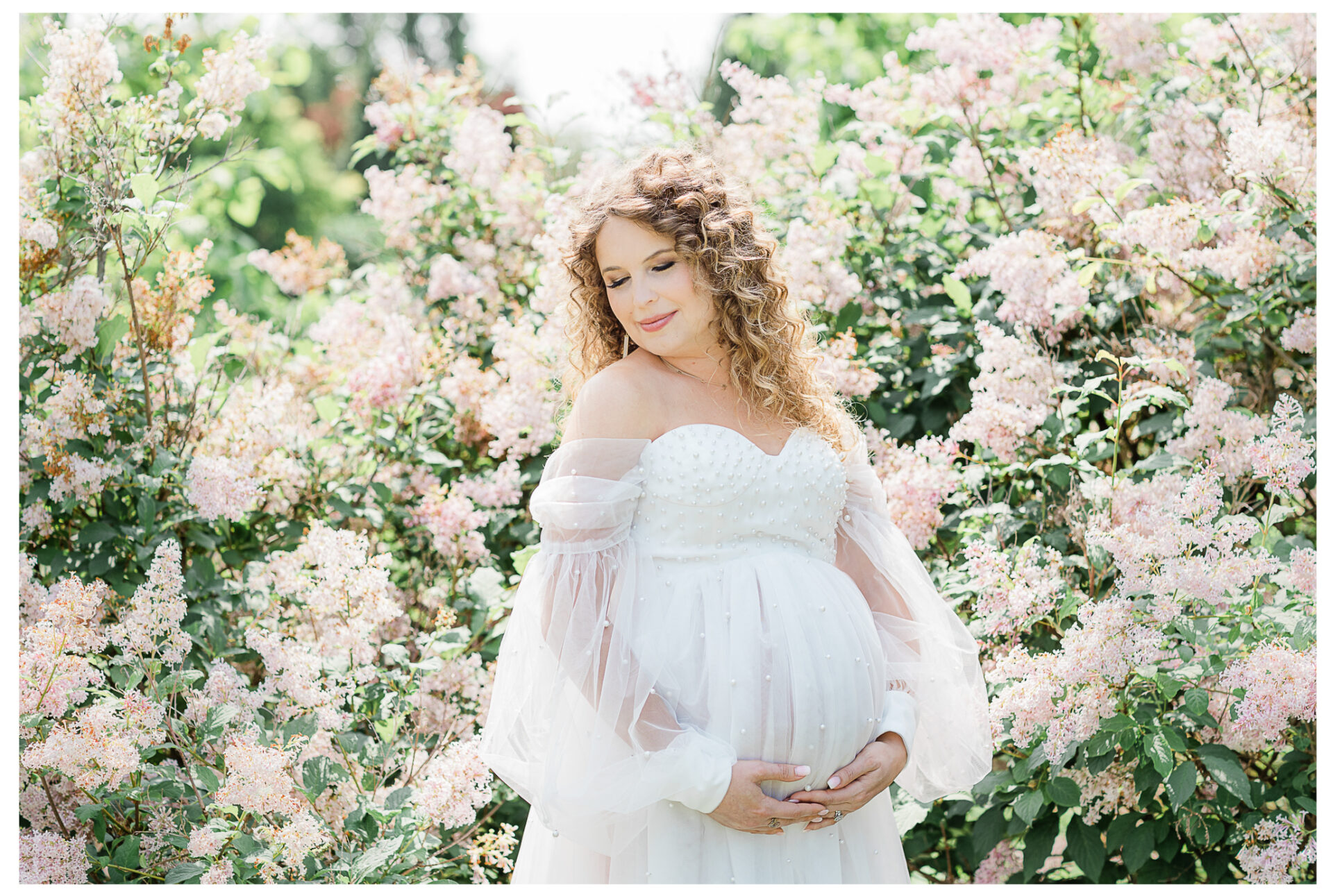 Winter Freire Photography | woman wearing a beautiful white gown during her outdoor summertime maternity session surrounded by blooming flowers