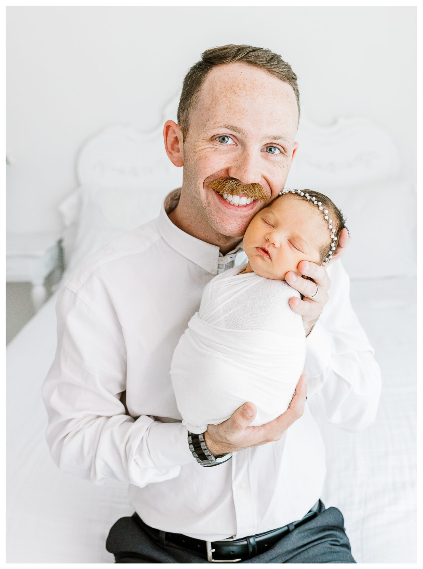Winter Freire Photography | Dayton, Ohio Newborn Session | Dad sitting on a bed while holding his newborn baby girl