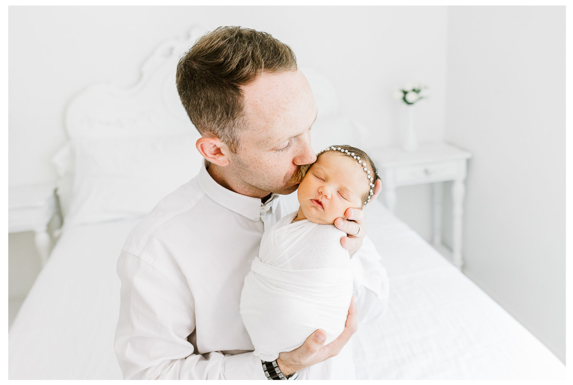 Winter Freire Photography | Dayton, Ohio Newborn Session | Dad sitting on a bed while kissing the cheek of his newborn baby girl