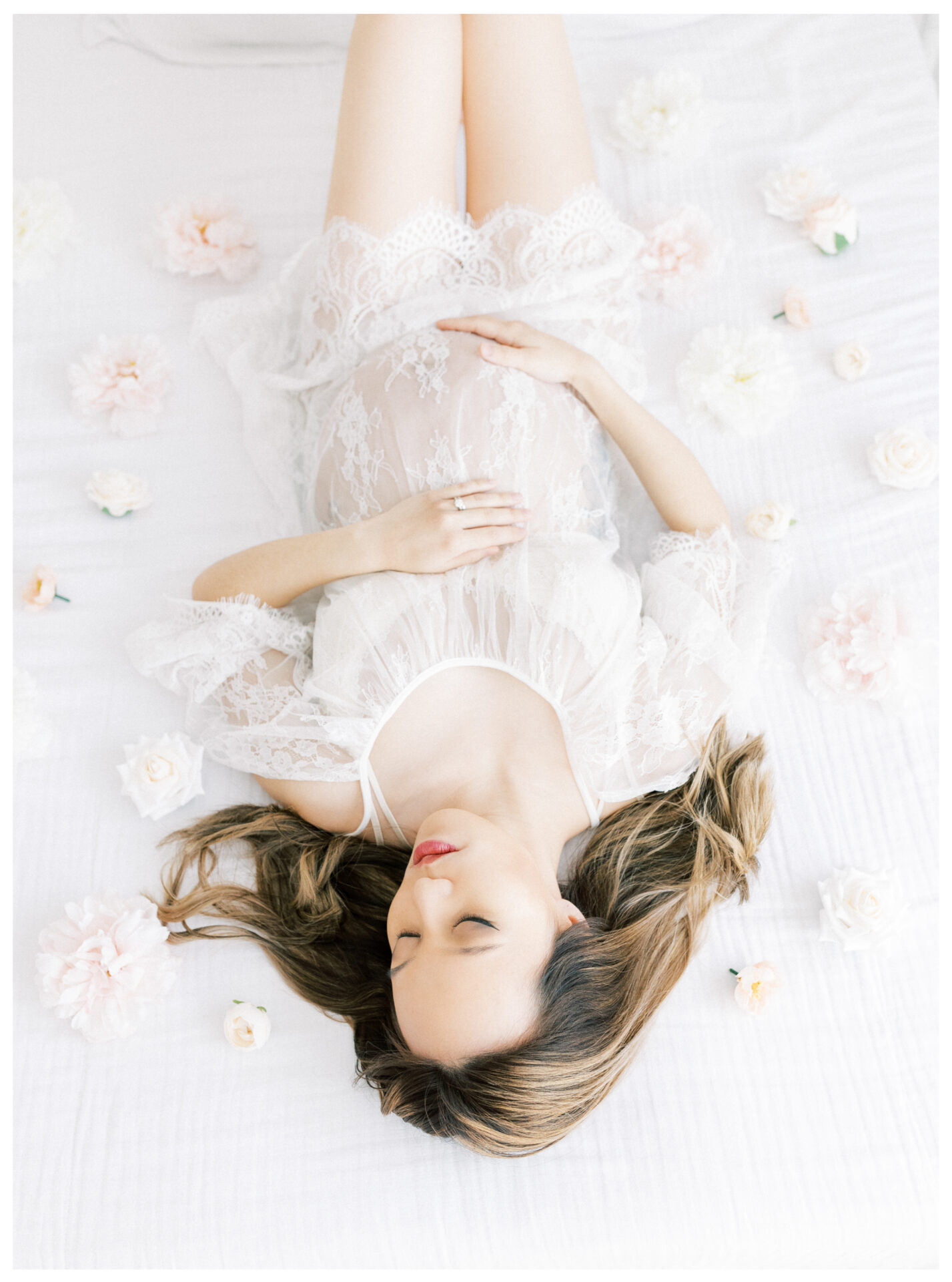 Winter Freire Photography | Fine Art Maternity Boudoir | Expecting mother wearing a sheer lace dress and laying on a beautiful white bed with flowers