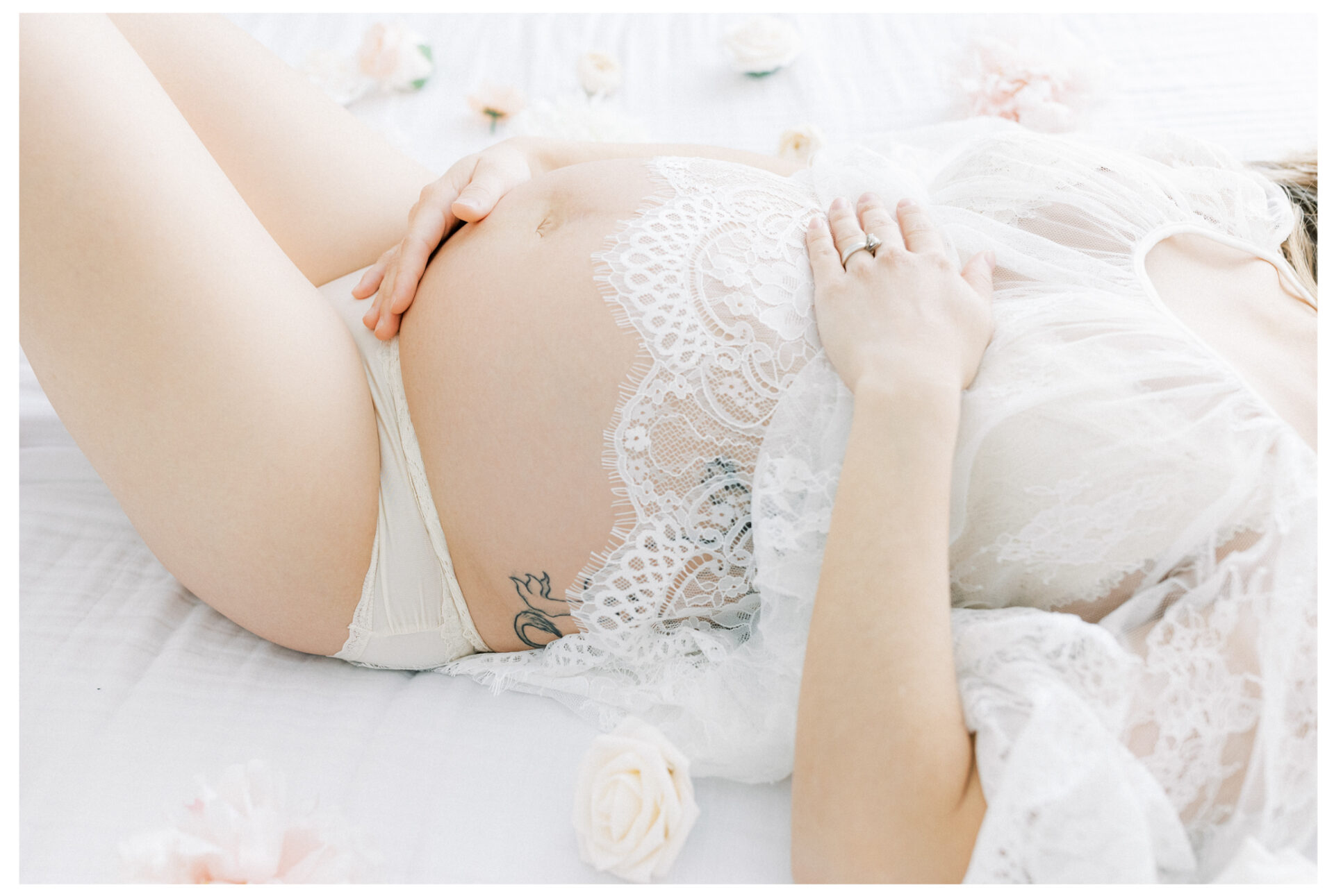 Winter Freire Photography | Fine Art Maternity Boudoir | Expecting mother wearing a sheer lace dress and laying on a beautiful white bed with flowers