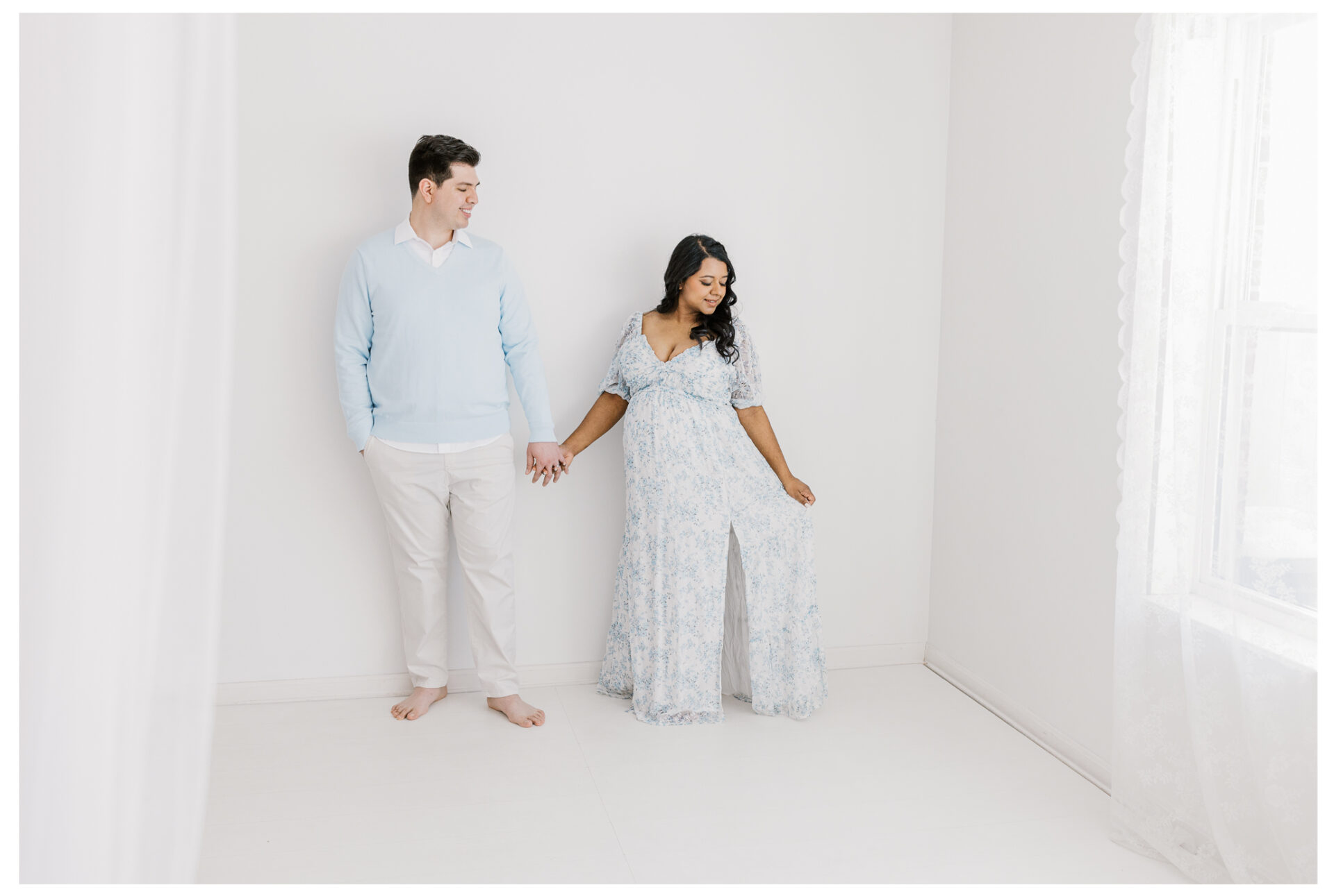 An expecting mother and her husband posing in front of.a white studio wall during a maternity session