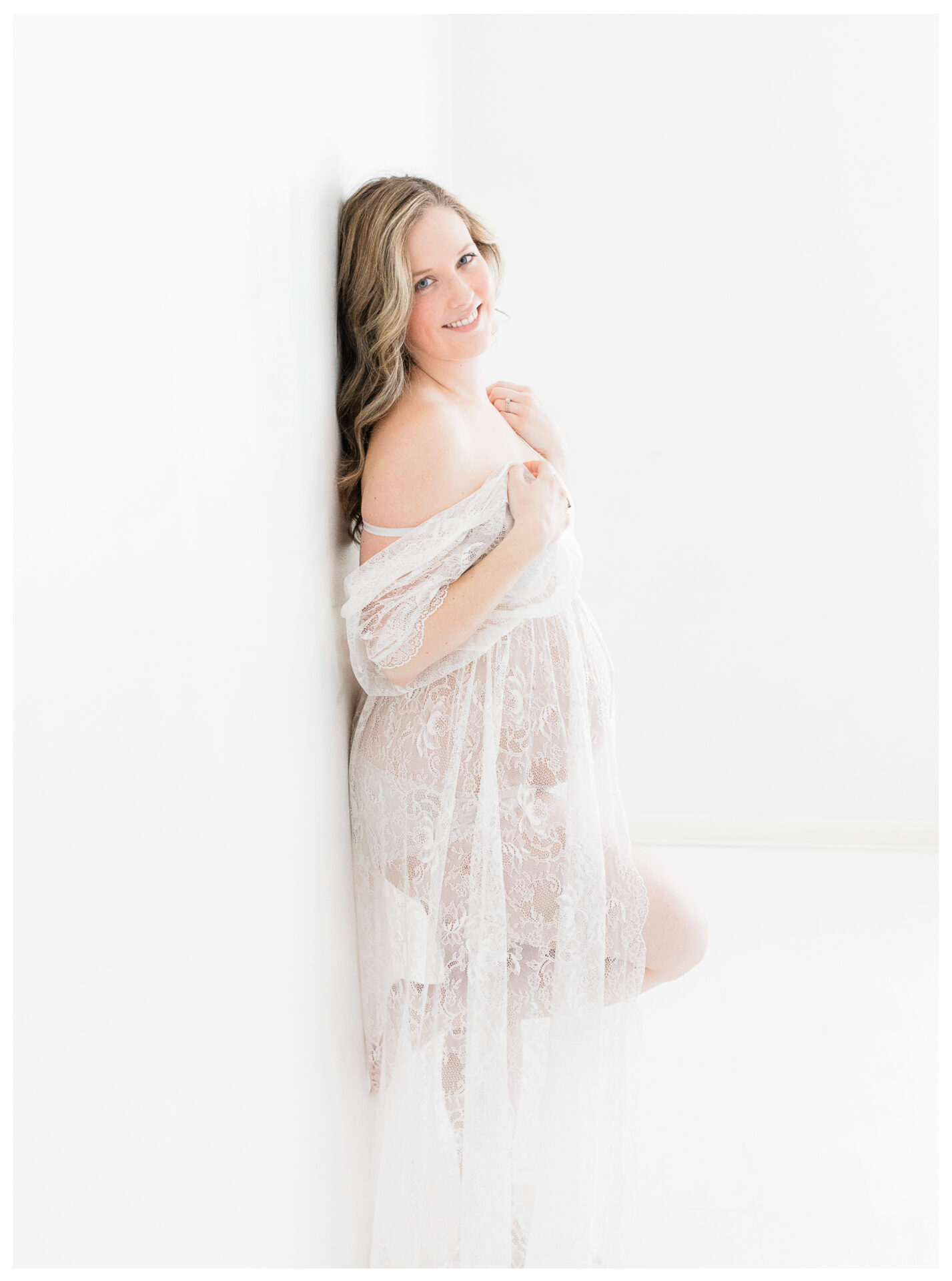 An expecting mother wearing a lace robe while smiling