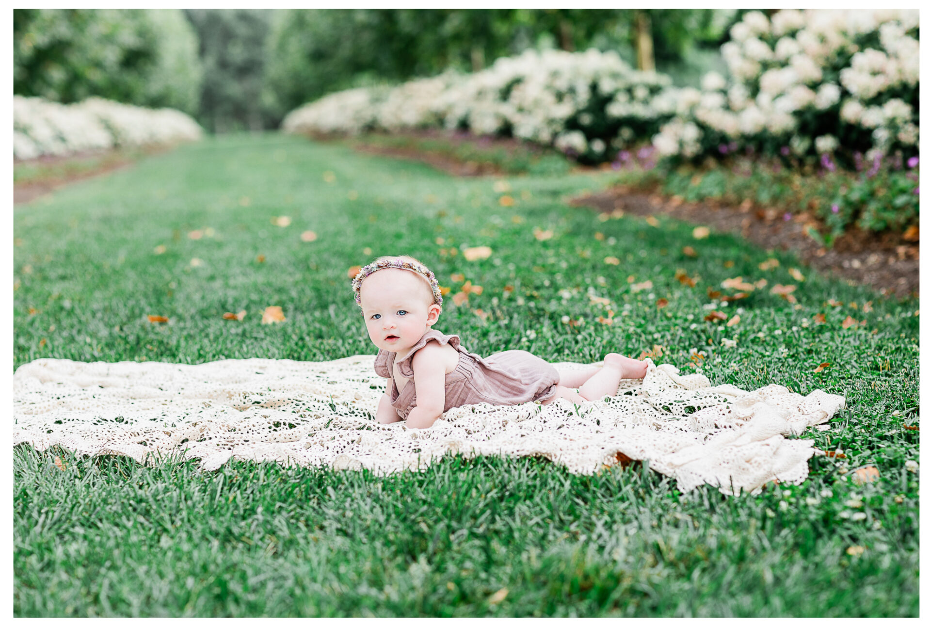 A baby girl lying on her tummy outside on a lace blanket.