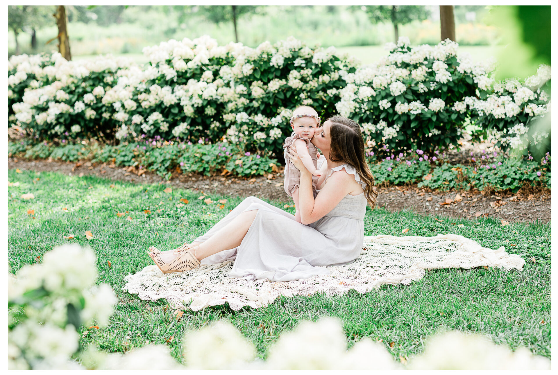 A mother sitting on a lace blanket kissing her youngest baby girl.