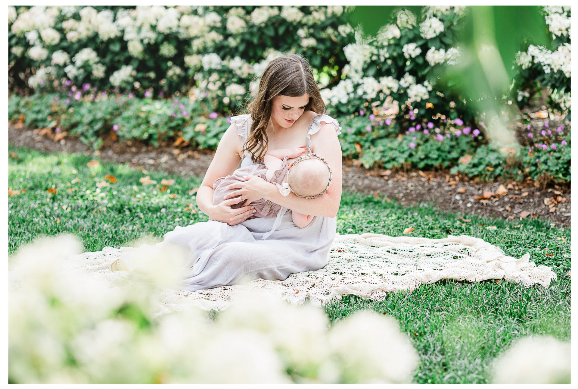A mother sitting on a lace blanket holding her youngest baby girl.