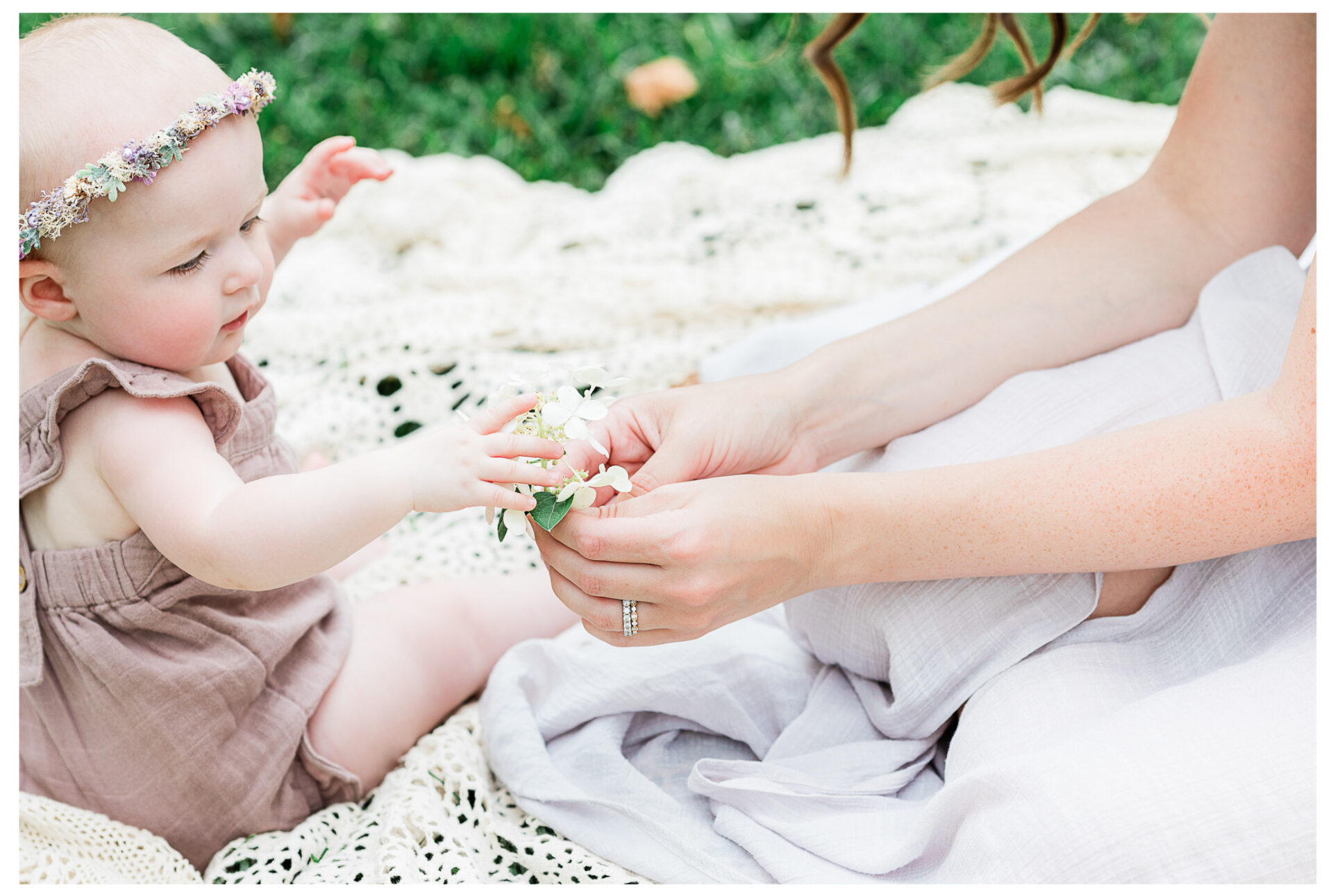 A close up of a baby's hands touching a flower that her mother is holding.
