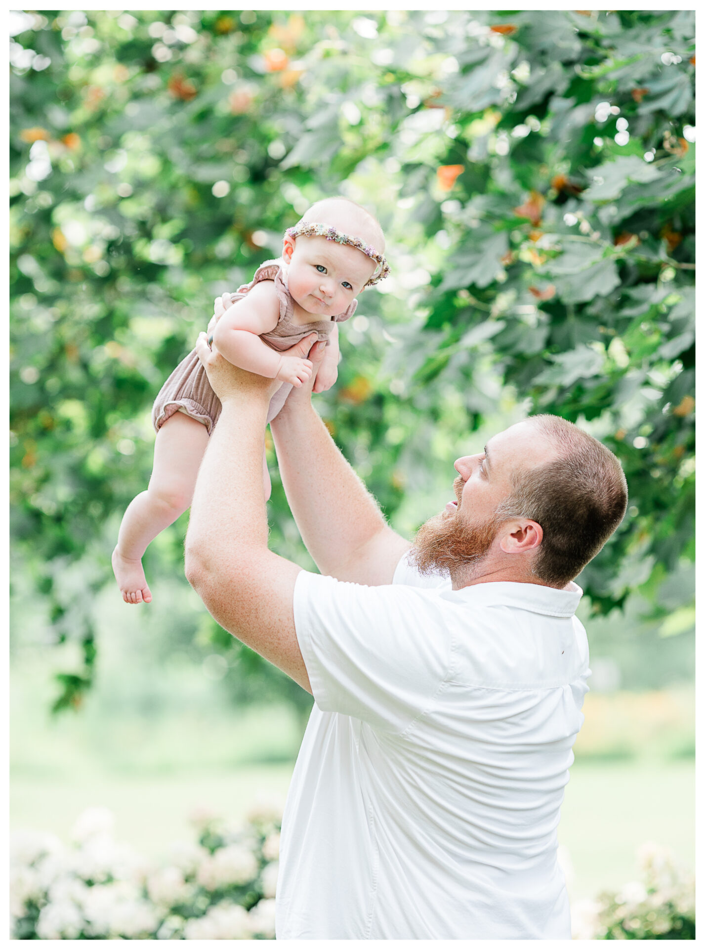 A father raising his baby daughter playfully in the air as she looks into the camera.