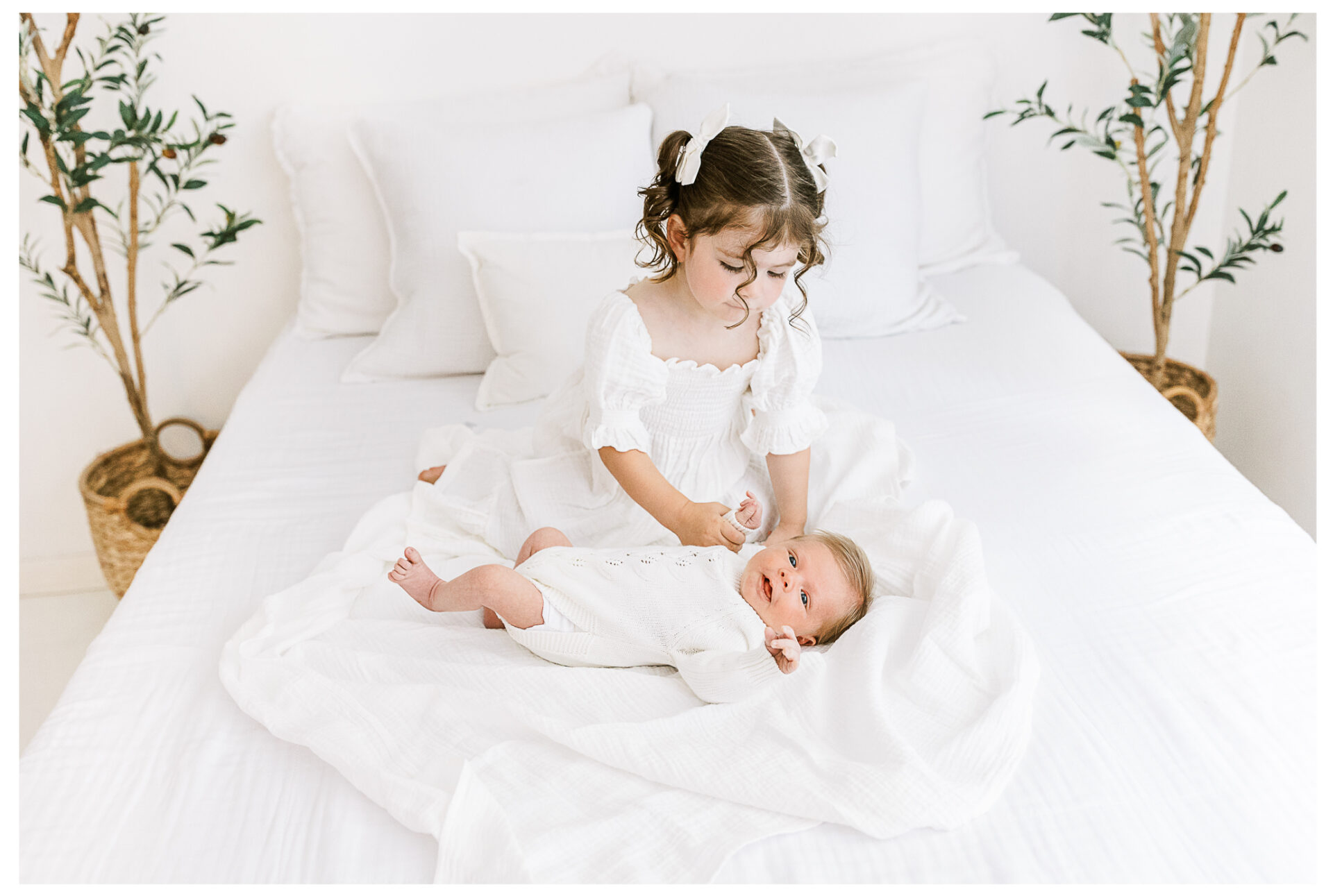 A toddler sister gently touching her newborn brother.