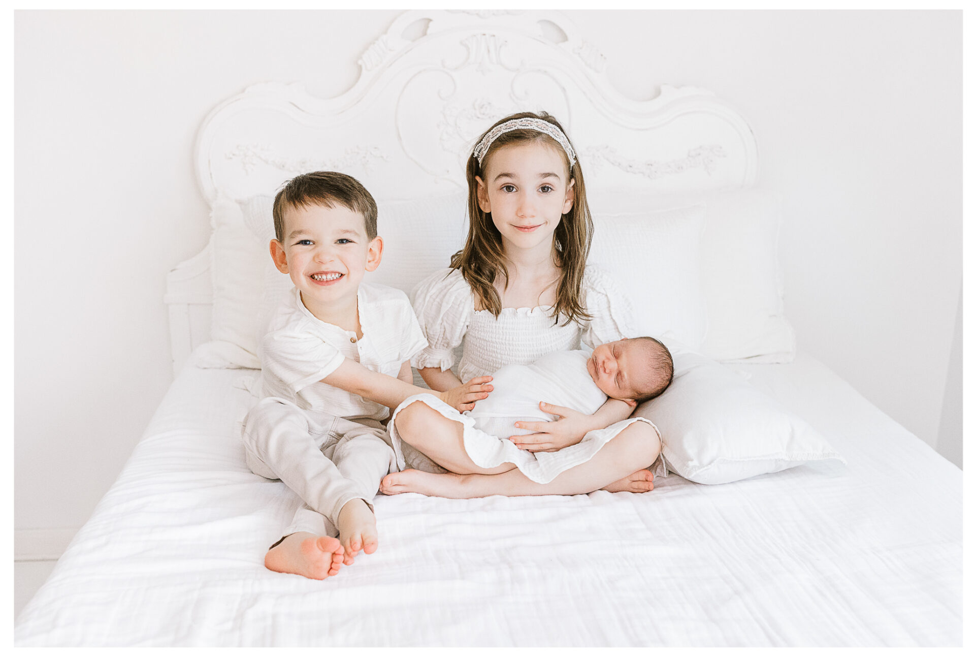 A young brother and sister smile as they hold their newborn brother.