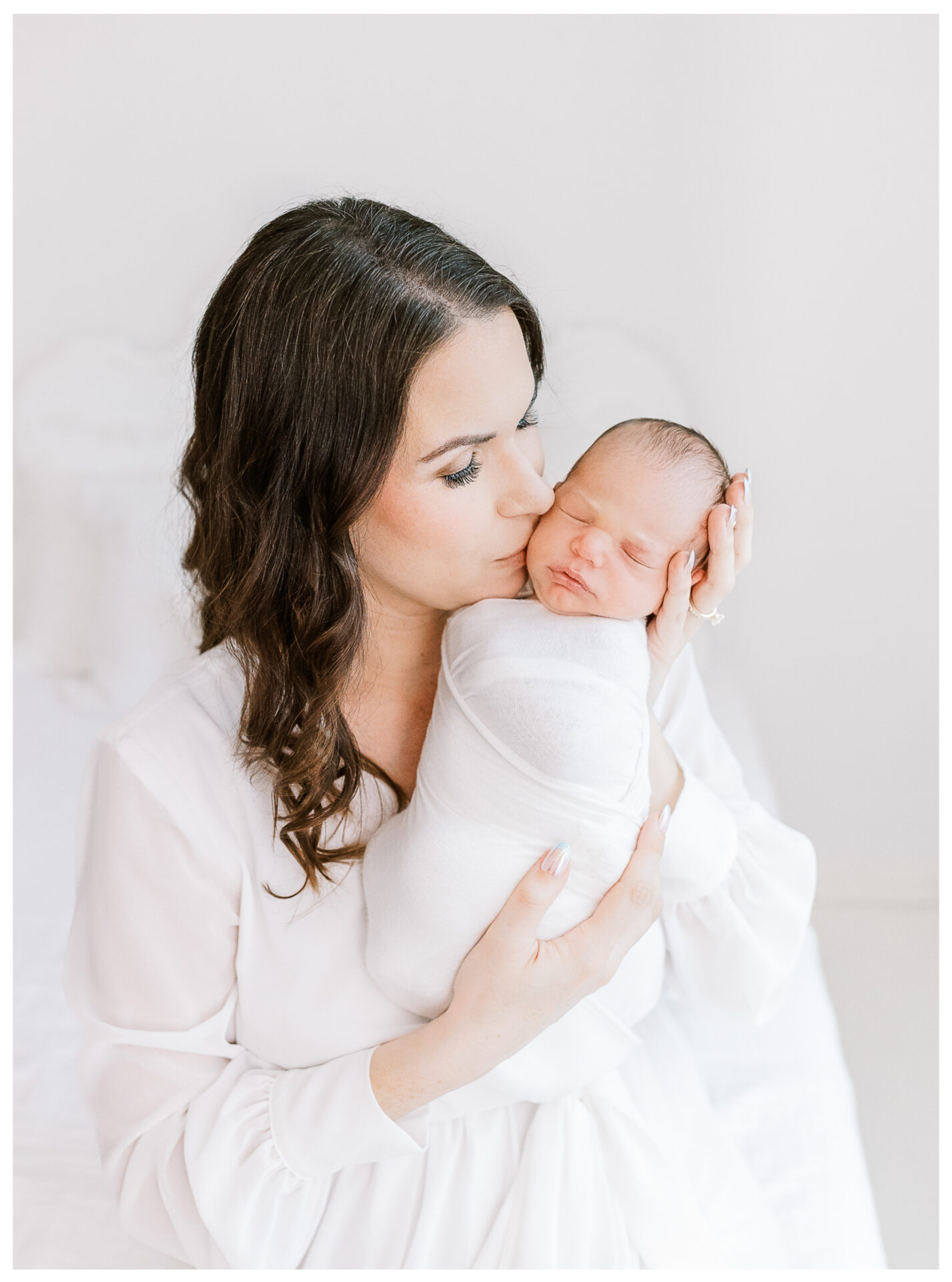 A mother giving her newborn son a gently kiss on his cheek.