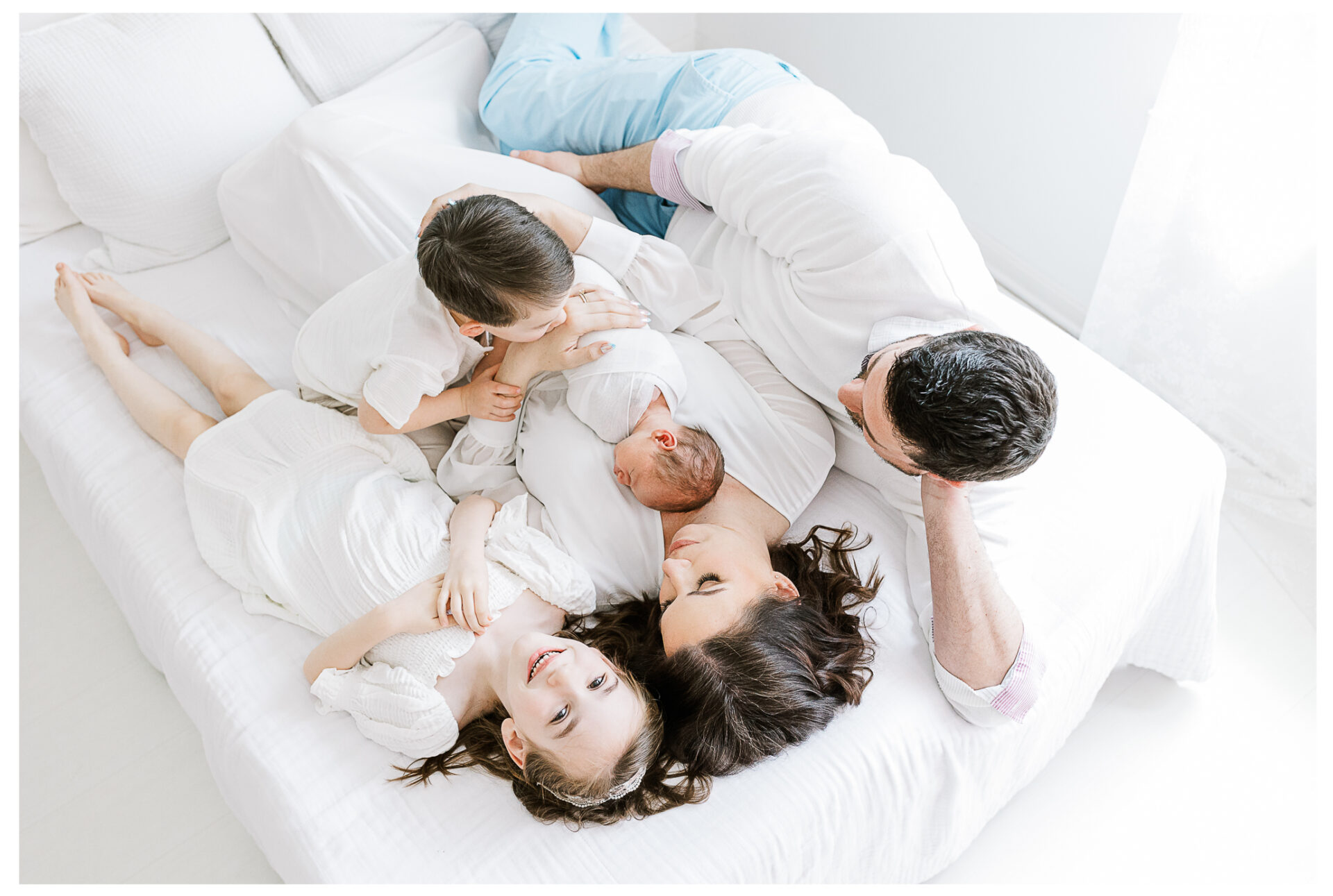 Parents with three young children lying together on a bed smiling and snuggling.
