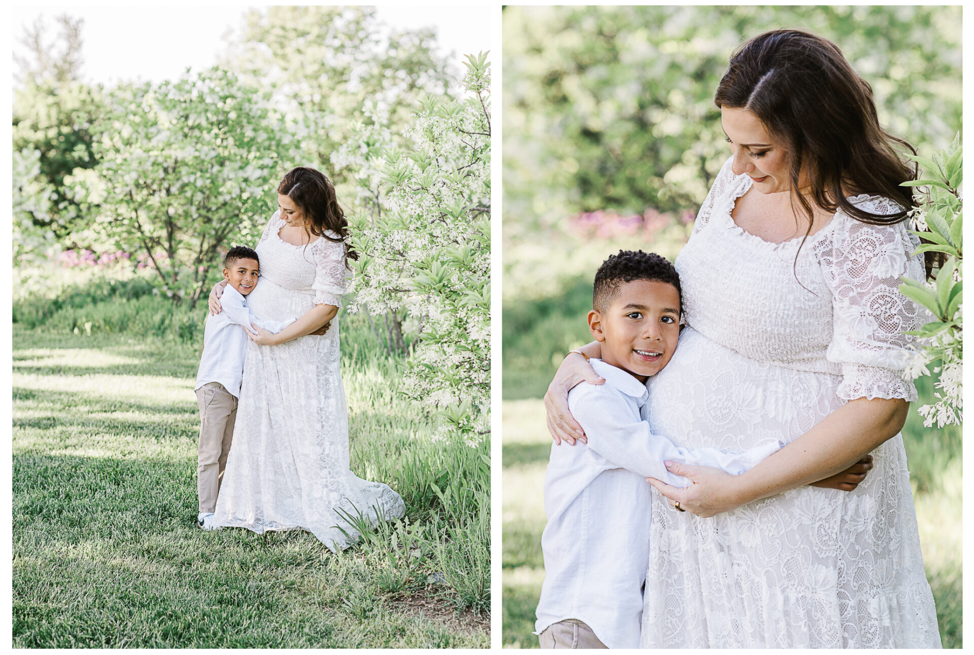 A pregnant mother in a white lace dress stands outdoors, lovingly hugging her young son who hugs her back. They are surrounded by lush green trees and grass, both smiling warmly at each other.